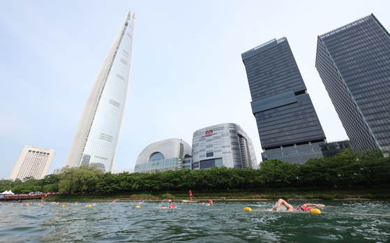 Competitors in the 2024 Lotte Aquathlon swim across Seokchon Lake in front of the Lotte World Tower in Songpa District, southern Seoul, in July. [NEWS1] 
