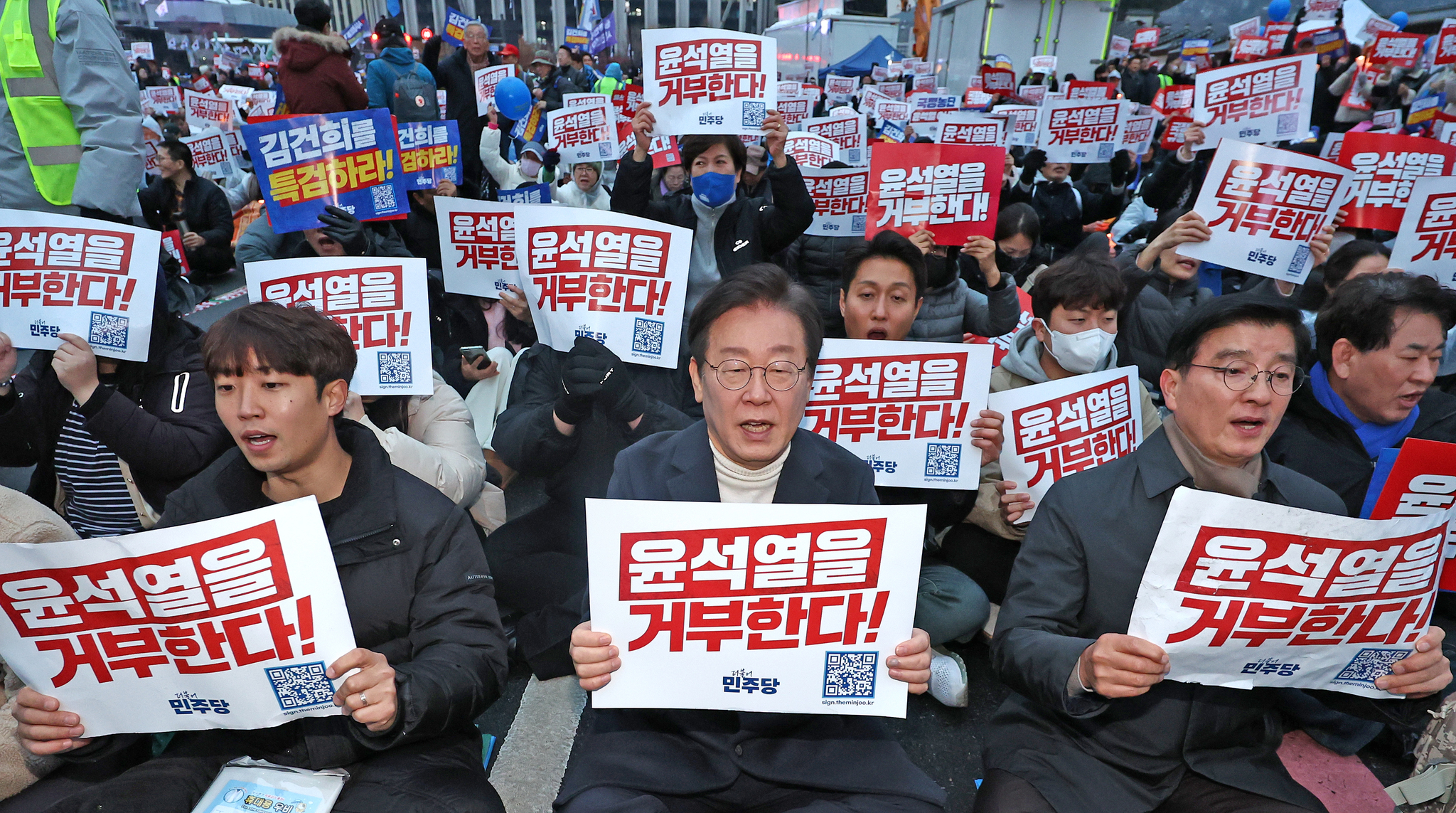 Lee Jae-myung, center, leader of the liberal Democratic Party, holds a picket saying ″Reject Yoon Suk Yeol″ in a rally held at Gwanghwamun Square in central Seoul on Saturday with other protesters. [NEWS1]