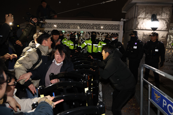 Officials at the National Assembly try to enter the building as police block the entrance late Tuesday night after President Yoon Suk Yeol declared emergency martial law. [JOONGANG ILBO]