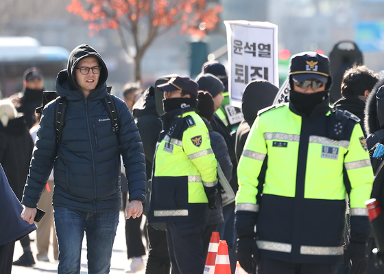 A foreigner, far left, walks by police positioned in Gwanghwamun in central Soul Wednesday, a day after President Yoon Suk Yeol's declaration of emergency martial law. [YONHAP]