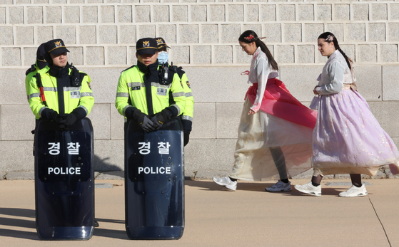 Foreign tourists wearing hanbok, or Korean traditional clothing, walk by police officers positioned in front of Gyeongbok Palace in central Seoul Wednesday, a day after President Yoon Suk Yeol's declaration of emergency martial law. [YONHAP] 