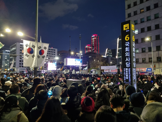 Protesters watch the news in front of the National Assembly complex in Yeouido, western Seoul, on Saturday. [KIM MIN-YOUNG]