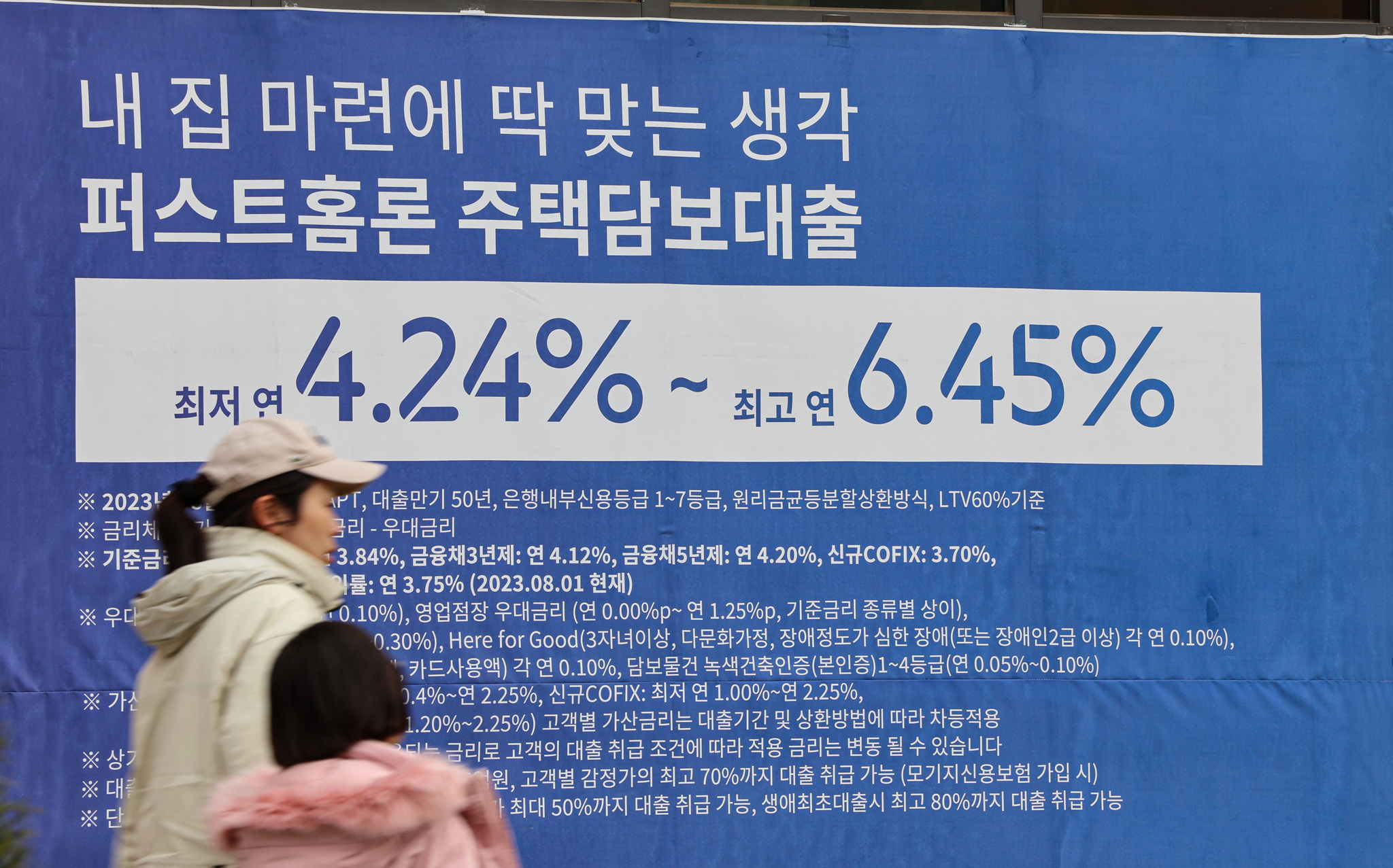 People walk past a sign about a bank's loan programs put up on the exterior of a lender in Seoul. [NEWS1] 
