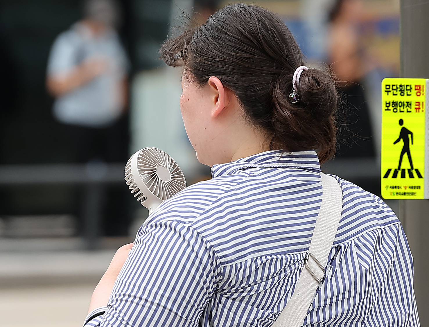 A woman uses a portable fan to beat the heat as she walks near Gwanghwamun in central Seoul on Aug. 11. [YONHAP] 