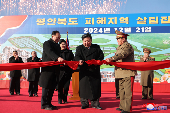 North Korean leader Kim Jong-un, center, cuts the ribbon at a ceremony held on Dec. 21 to mark the completion of rebuilt houses previously destroyed by floods in North Pyongan Province in July, in this photo released by the North's official Korean Central News Agency the next day. [YONHAP]