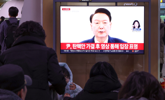 Travelers watch the news on the parliamentary impeachment motion vote against President Yoon Suk Yeol on a television in Seoul Station on Dec. 14. [YONHAP]