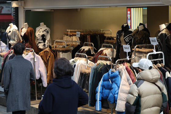 Shoppers pass by racks of coats and jackets in the Myeong-dong shopping district in central Seoul on Sunday. [YONHAP]