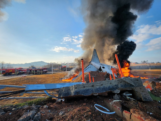 Smoke and flame billow from the debris of a Jeju Air passenger plane that collided with a perimeter wall after crash-landing at Muan International Airport in South Jeolla on Dec. 29. [YONHAP] 