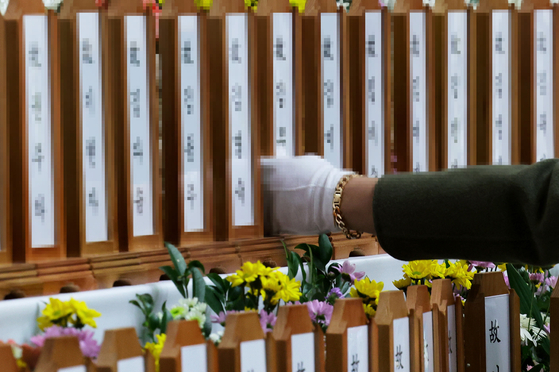 A bereaved family member of the victims of Sunday’s Jeju Air crash touches one of the memorial plaques with the names of the victims at a memorial altar set up in Muan Sports Complex in Muan, South Jeolla, on Monday. [JOONGANG ILBO] 