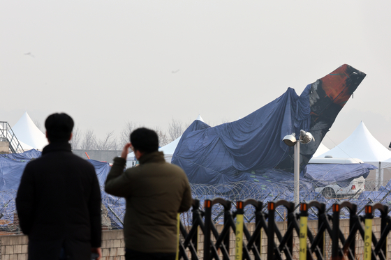 A waterproof tarp covers the tail section of the destroyed Jeju Air plane to protect it from the rain at Muan International Airport in South Jeolla on Monday. [YONHAP]