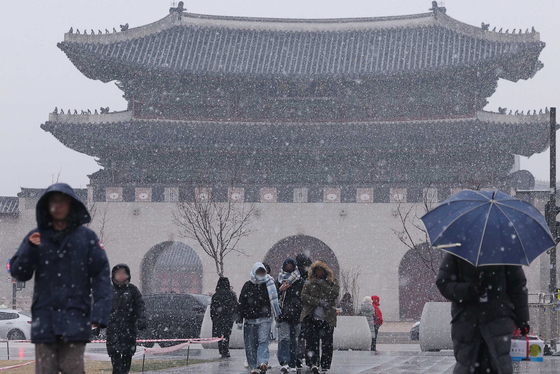  People walk as it snows at Gwanghwamun Square in Jongno District, central Seoul, on Jan. 13. Snow and rain will continue through the morning of Jan. 14 in Seoul, with temperatures dropping to a low of minus 5.6 degrees Celsius (21.9 degrees Fahrenheit).[YONHAP]