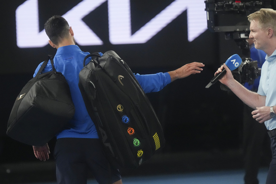 Novak Djokovic hands microphone to Jim Courier after declining to do a customary post-match interview at the Australian Open tennis championship in Melbourne, Australia, Sunday, Jan. 19, 2025. [AP/YONHAP]