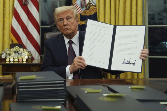 U.S. President Donald Trump holds up an executive order commuting sentences for people convicted of Jan. 6 offenses in the Oval Office of the White House in Washington, Jan. 20, [AP/YONHAP]