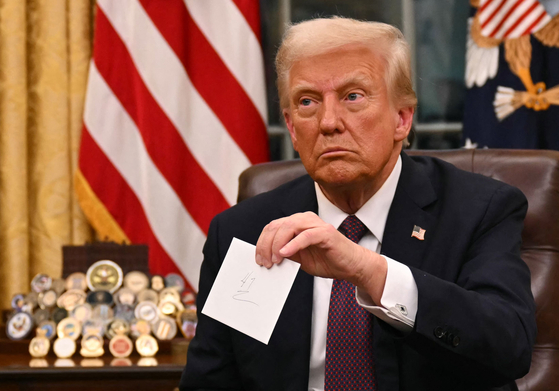 U.S. President Donald Trump holds up outgoing President Joe Biden's letter as he signs executive orders in the Oval Office of the White House in Washington on Jan. 20. [AFP/YONHAP]
