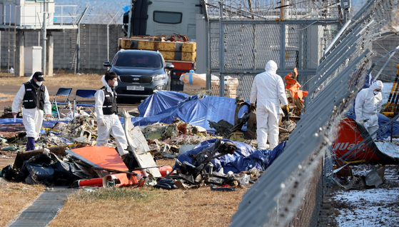 Members of a government joint investigation team, including Transport Ministry’s Aviation and Railway Accident Investigation Board (Araib), inspect the area around the tail wing of the crashed passenger plane at the sie of the Jeju Air crash at Muan International Airport on Jan. 8. [YONHAP]