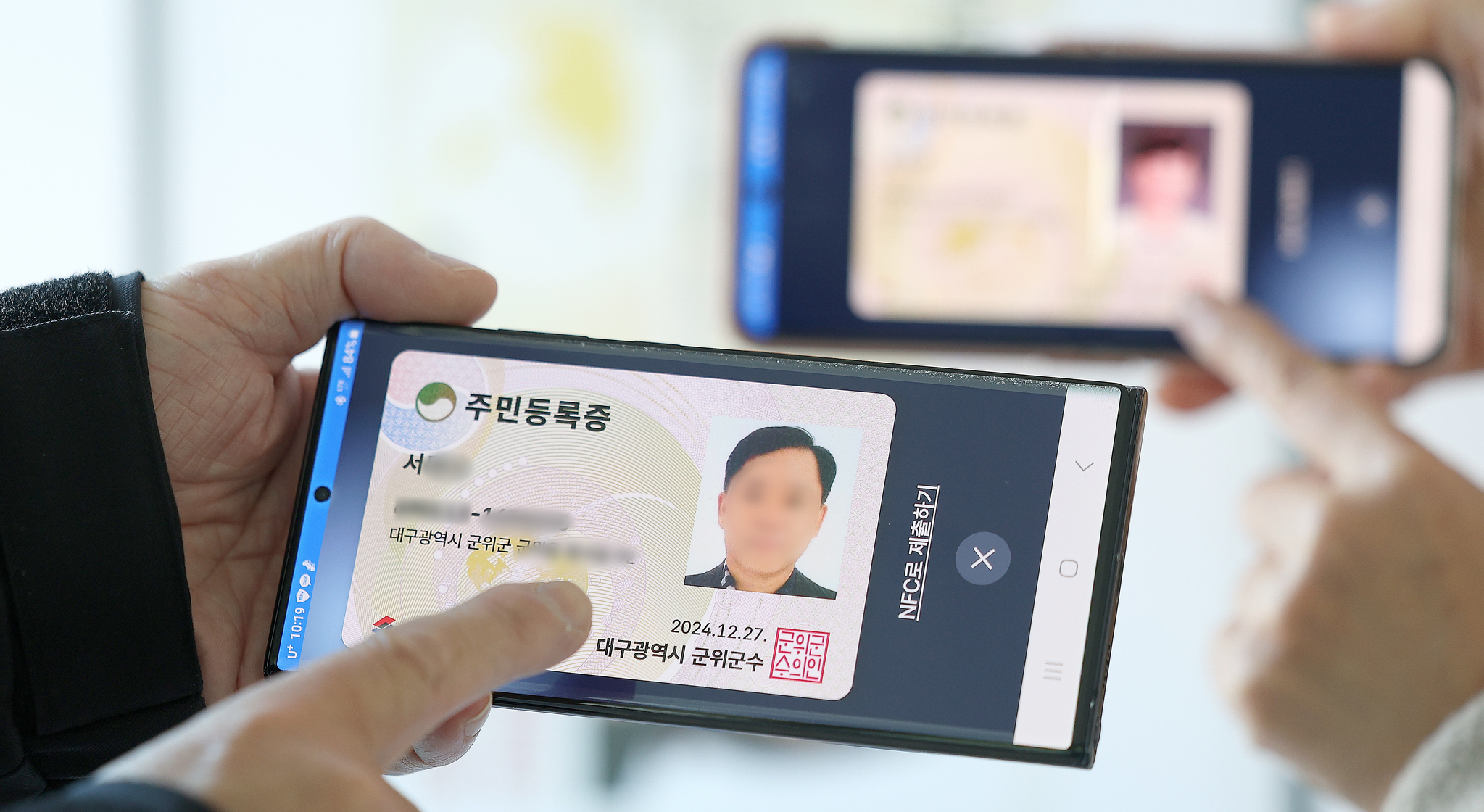A person holds up a mobile device displaying an electronic copy of a residence registration card at a community center in Gunwi County, Daegu, in December last year. [YONHAP]  
