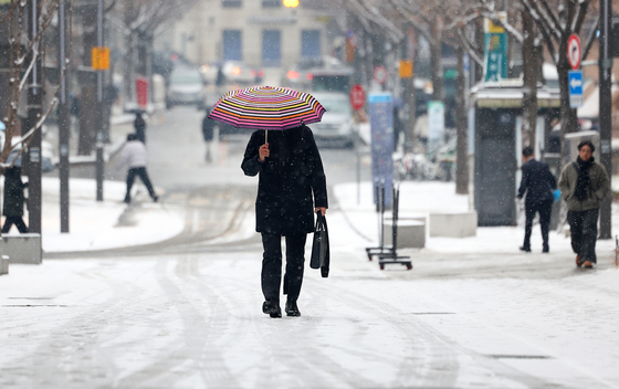 A person walks on a snow covered street holding an umbrella in Jongno District, central Seoul, on Feb. 12. [YONHAP]