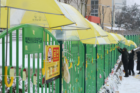 Umbrellas are attached on a fence at an elementary school on Feb. 12 in Daejeon where a 7-year-old girl was stabbed to death. Letters, flowers and dolls given by visitors who paid condolence visits are placed along the fence. [YONHAP] 