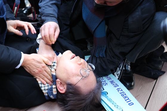 Democratic Party leader Lee Jae-myung lies on the ground after being stabbed in his neck during a visit to observe the new airport site on Gadeok Island, Busan, on Jan. 2, 2024. [YONHAP]