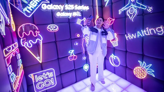 A visitor poses for a photo at the Galaxy S25 photo zone of the Galaxy Studio, featuring neon art displays. [SAMSUNG ELECTRONICS]
