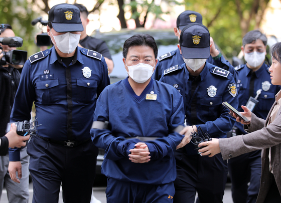 Police officers escort Ra Deok-yeon, who was indicted for stock price manipulation, at the Seoul Southern District Court in Yangcheon District, western Seoul, on May 11, 2023. [NEWS1] 