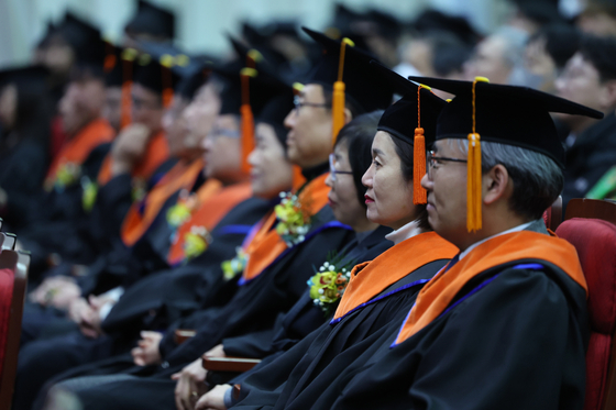 Alumi of Korea Polytechnics listen to congratulary messages at its graduation ceremony. [YONHAP]