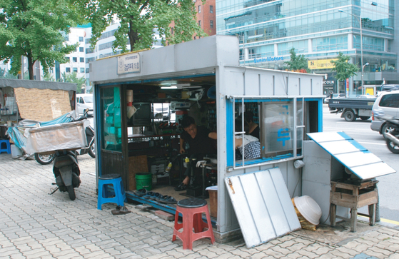 A man works at a shoe repair stand with a design from before standardization. [SEOUL METROPOLITAN GOVERNMENT] 