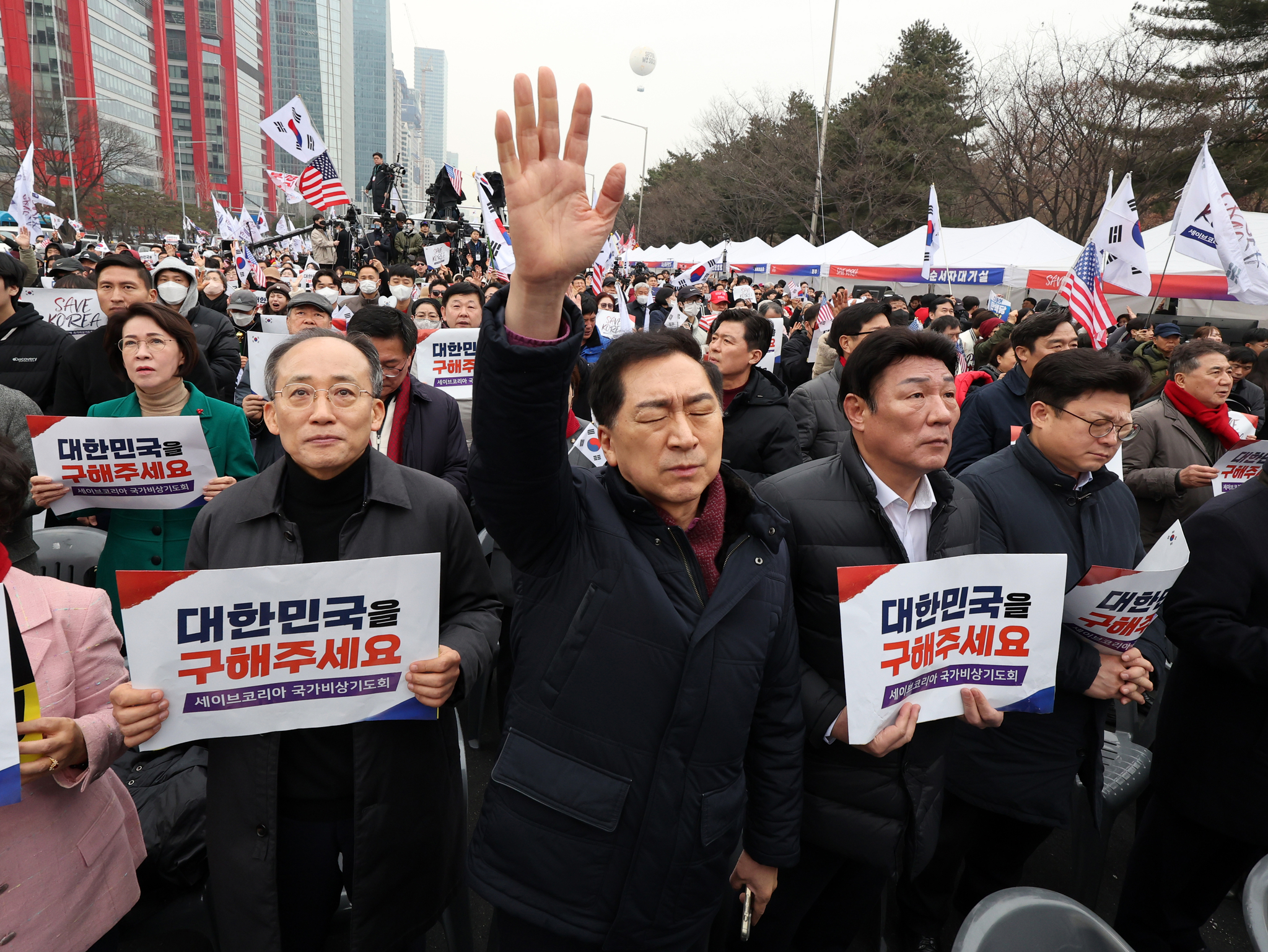 Conservative People Power Party (PPP) Rep. Kim Gi-hyeon, center, raises his hands in prayer at a rally in Yeouido, western Seoul, on March 1. PPP Rep. Choo Kyung-ho, left, holds up a placard that says ″Please save Korea.″ [NEWS1]