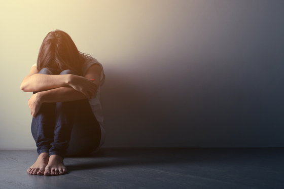 Teenager girl sitting alone on the floor in the dark room. [SHUTTERSTOCK]