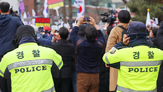 Two police officers stand in front of demonstrators protesting the impeachment of President Yoon Suk Yeol at a rally site in Jongno Distict in central Seoul last month. [YONHAP]  