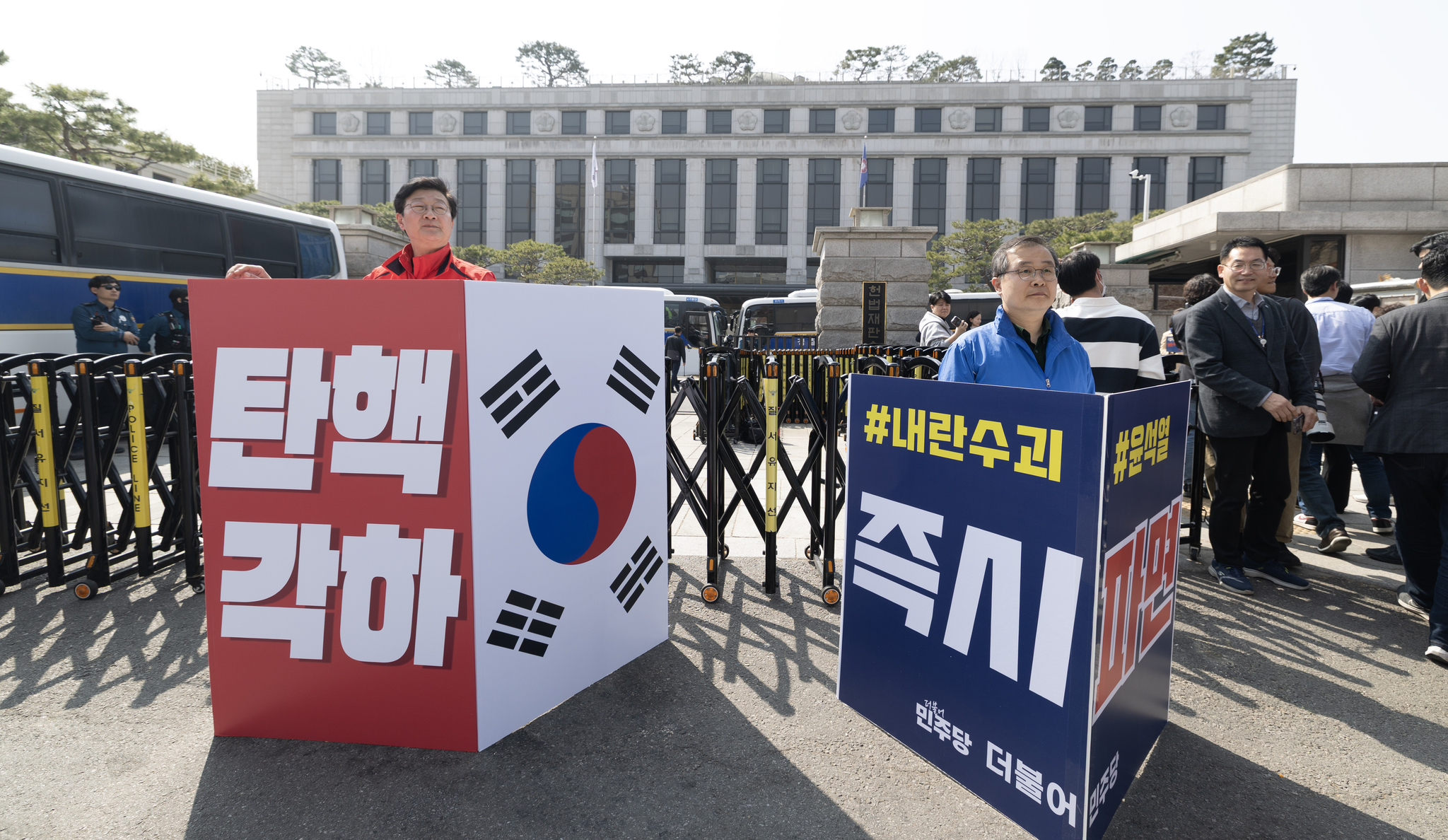 An official from the conservative People Power Party, left, holds a sign calling for President Yoon Suk Yeol's reinstatement, while a member of the liberal Democratic Party, right, holds a sign calling for his removal from office in front of the Constitutional Court in Jongno District, central Seoul, on March 23. [NEWS1]