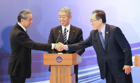 South Korean Foreign Minister Cho Tae-yul, right, shakes hands with Chinese Foreign Minister Wang Yi, left, as Japanese Foreign Minister Takeshi Iwaya watches on, during the trilateral meeting between the three ministers in Tokyo on March 21. [YONHAP]