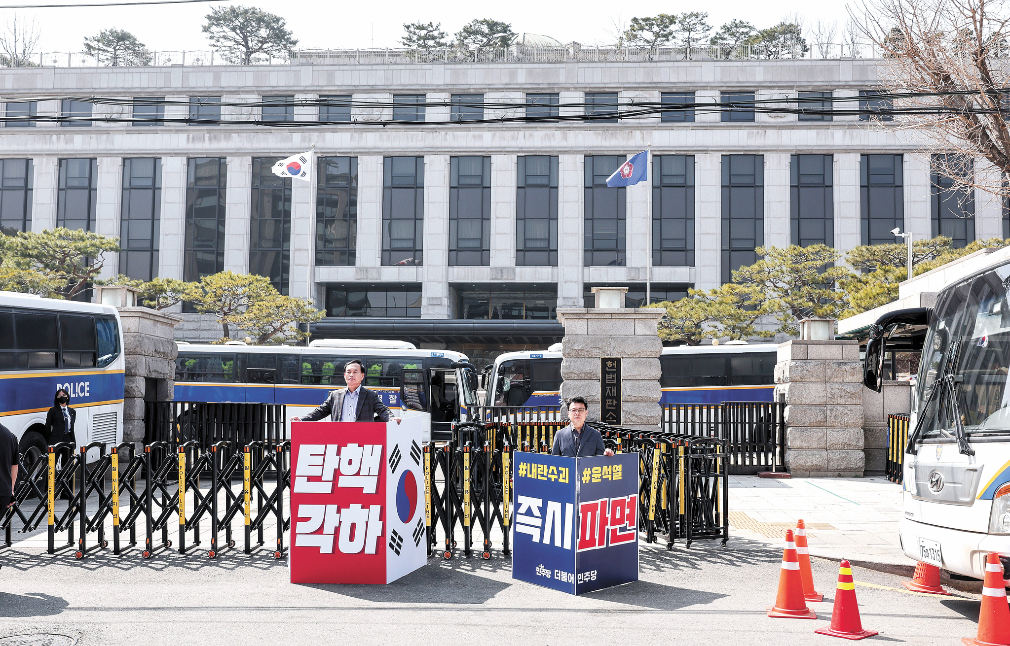 An official from the conservative People Power Party, left, holds a sign calling for President Yoon Suk Yeol's reinstatement, while a member of the liberal Democratic Party, right, holds a sign calling for his removal from office in front of the Constitutional Court in Jongno District, central Seoul, on March 23. [JOONGANG ILBO]