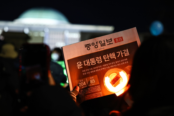 A person holds up a copy of the JoongAng Ilbo after the impeachment motion against President Yoon Suk Yeol was passed by the National Assembly in Yeouido, western Seoul, on Dec. 14. [JOONGANG ILBO] 
