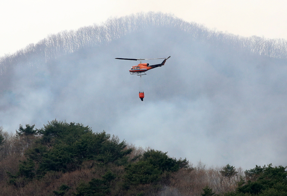 A helicopter equipped for firefighting flies over a wildfire in Hadong, South Gyeongsang on March 28. [NEWS1]