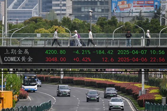 People walk across a bridge with a stocks indicator board in the financial district of Shanghai on April 7. [AFP/YONHAP]