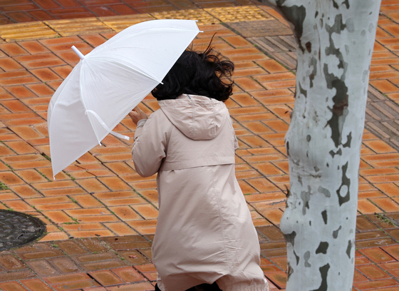 A passerby holds firmly onto her umbrella due to strong winds in Gwangju on April 14. [YONHAP]