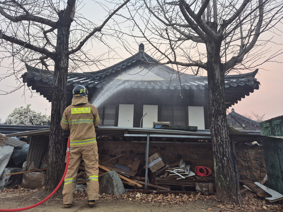 A firefighter sprays water on a traditional Hanok house in Hahoe Village in Andong on March 26. [PARK JIN-HO]