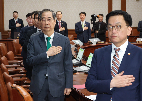 Acting President Han Duck-soo, left, and Minister of Economy and Finance Choi Sang-mok, right, pledge allegiance to the flag before a Cabinet meeting to review the supplementary budget plan for this year at the government complex in Jongno District, central Seoul on April 18. [JOINT PRESS CORPS] 