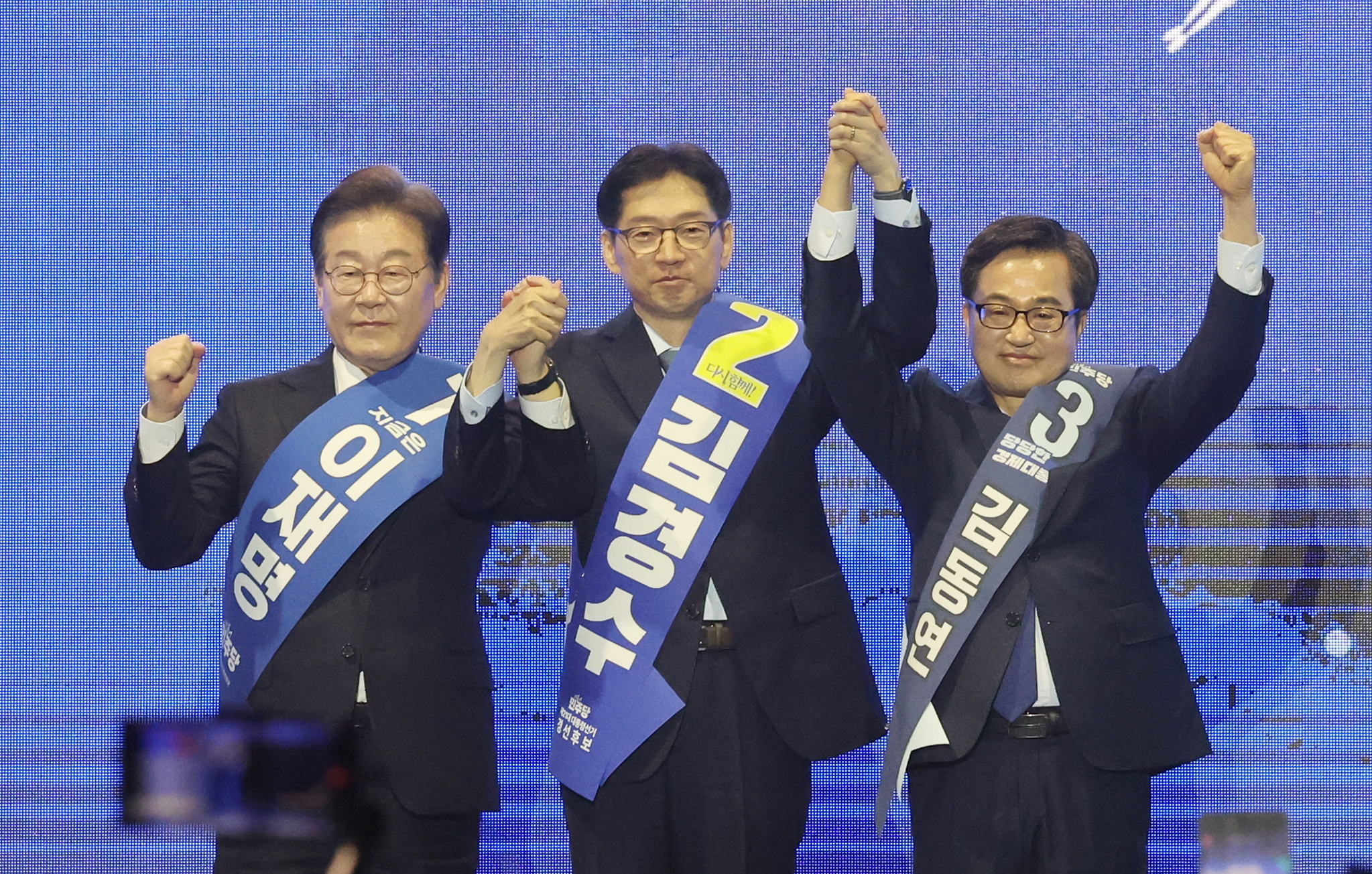 From left, Democratic Party presidential candidates Lee Jae-myung, Kim Kyoung-soo and Kim Dong-yeon hold hands and pose for a photo during a regional primary for the Gyeongsang region in Ulsan on April 20, ahead of the June 3 presidential election. [YONHAP] 