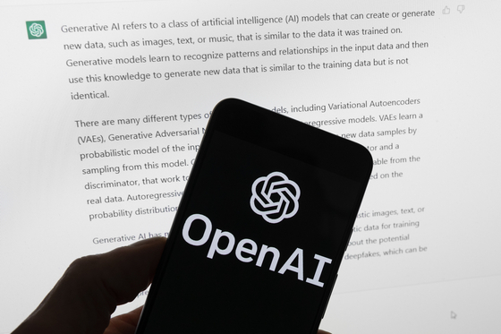 The OpenAI logo is seen on a mobile phone in front of a computer screen displaying output from ChatGPT in Boston on March 21, 2023. [AP/YONHAP]