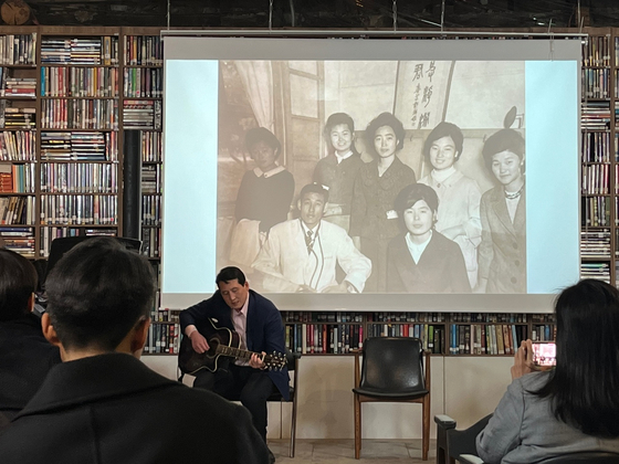 James Rhee singing a song that his father used to enjoy, with a photo of his mother in the background. [JAMES RHEE]