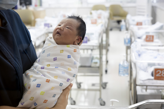 A newborn is held by a nurse at a hospital in Gangseo District, western Seoul, on Feb. 26. [JUN MIN-KYU]