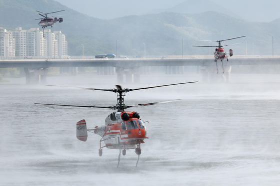 Helicopters from the Korea Forest Service and fire authorities collect water from the nearby Geumho River on May 1 to fight the rekindled wildfire on Mount Hamji in Buk District, Daegu, after it was brought under control on April 29. [YONHAP]