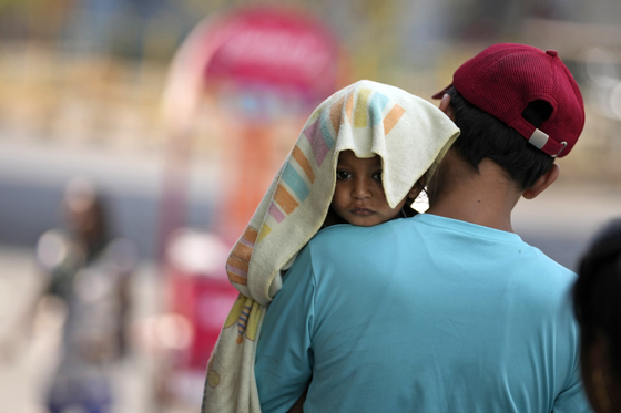 A man carries a child, head covered with a towel to protect from the heat, in Jammu, India, on June 2, 2024. [AP/YONHAP]