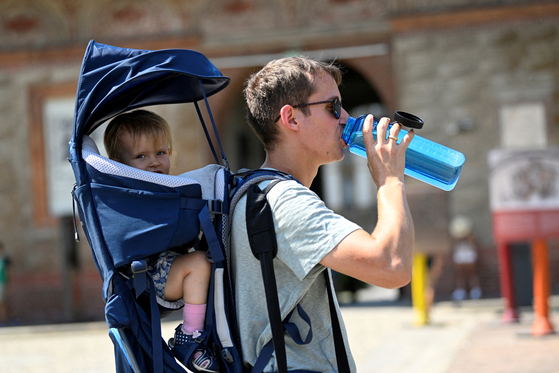 A man carrying a baby drinks water as another heatwave hits Milan, Italy, on Aug. 5, 2022. [REUTERS/YONHAP]