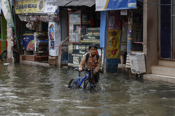 A child pushes his bicycle through high-tide floodwater on a street in North Jakarta, Indonesia, on Nov. 20, 2024. [EPA/YONHAP]