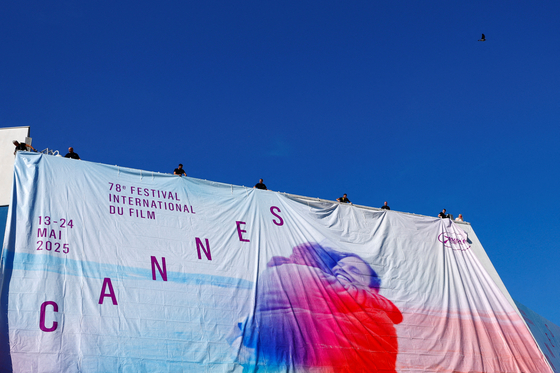 Workers set up a giant canvas of one of the official double poster featuring a joint tribute to the two actors Anouk Aimee and Jean-Louis Trintignant in the film ″A Man and a Woman″ on the Festival Palace ahead of the opening ceremony of the 78th Cannes Film Festival in Cannes, France, May 11. [REUTERS/YONHAP]