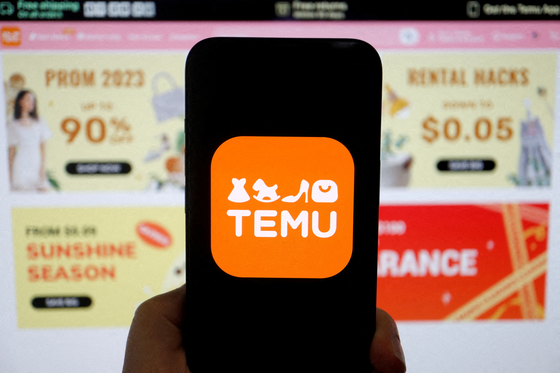 The logo of Chinese e-commerce platform Temu is seen on a mobile phone displayed in front of its website. [REUTERS/YONHAP]