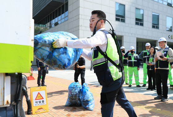 Dobong District Mayor Oh Un-seok wears a wearable robot device while lifting up trash bags at a demonstration event held at the district office plaza on May 14. [DOBONG DISTRICT OFFICE]